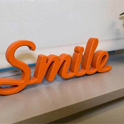 Bright orange "Smile" word decoration sitting on a shelf in an orthodontic office setting.