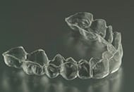 Clear orthodontic aligner tray displayed against neutral gray background, showing dental correction device.