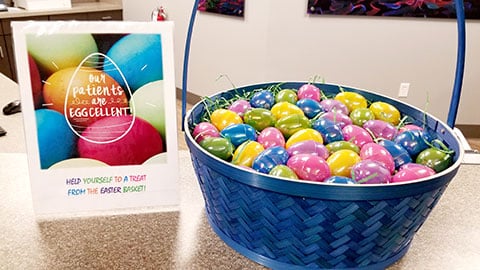 Colorful lollipops in blue basket next to orthodontic office branding on white counter.