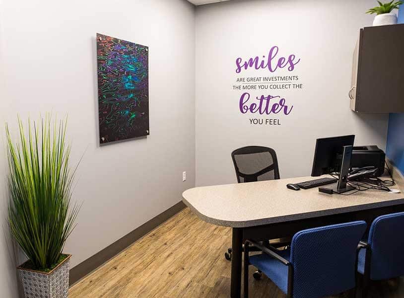 Modern orthodontic office waiting area with desk, chairs, plant, and motivational wall decor.