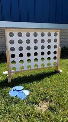 Giant Connect Four game on grass with blue game piece in foreground, brick building background.