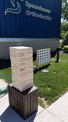 Outdoor Jenga and cornhole games displayed on grass in front of Spoonhower Orthodontics building.
