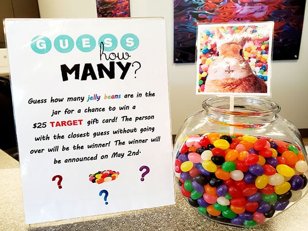 Guess How Many jelly beans game display with colorful candies in glass jar and contest rules poster.
