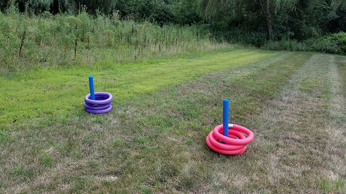 Two colorful ring toss games set up on a grassy lawn with trees in background.