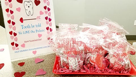 Valentine's Day orthodontic care package with pink hearts, branded card, and red heart-shaped candies displayed on white surface.