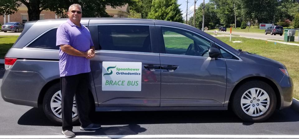 Man standing beside gray minivan with Spoonhower Orthodontics sign in parking lot.